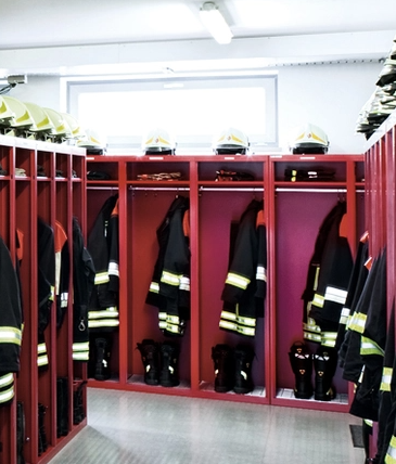 Vestiaires de pompiers avec uniformes et casques suspendus dans des armoires rouges.