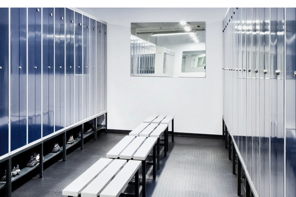 Vestiaire moderne avec bancs et casiers bleus, murs clairs et miroir.